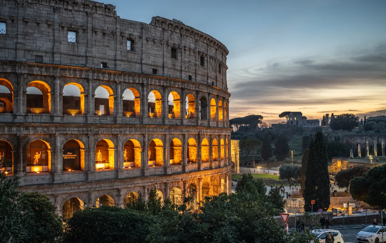 The Colosseum in Rome at dusk, its arched levels lit against an evening sky